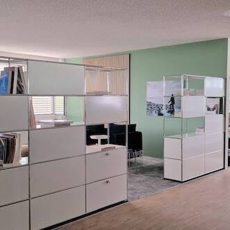 Einladend und modern gestaltetes USM-Bücherregal im Büro mit Holzpaneelen, grün-grauem Ambiente von der Natur inspiriert.