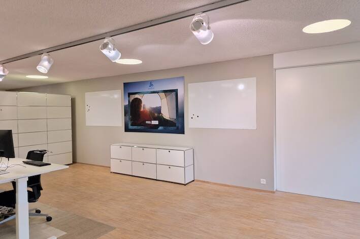 Geräumiger Projektraum mit Whiteboards, höhenverstellbaren Schreibtischen und modernen Drehstühlen für produktives Arbeiten.