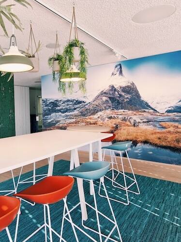 Work Café mit grossem XXL Bild und roten und blauen Hochstühlen. Kreativer Arbeitsplatz mit inspirierender Atmosphäre.