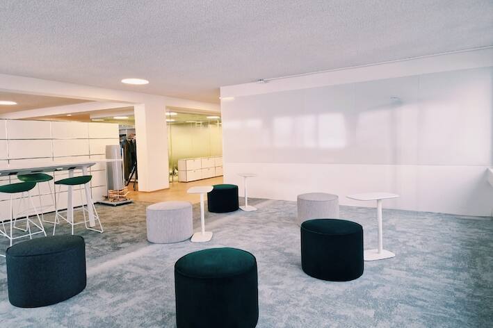 Innovations-Raum mit grauem Interface Teppich, praktischen Laptop-Tischen, grünen und grauen Sitzhocker, Whitewall
